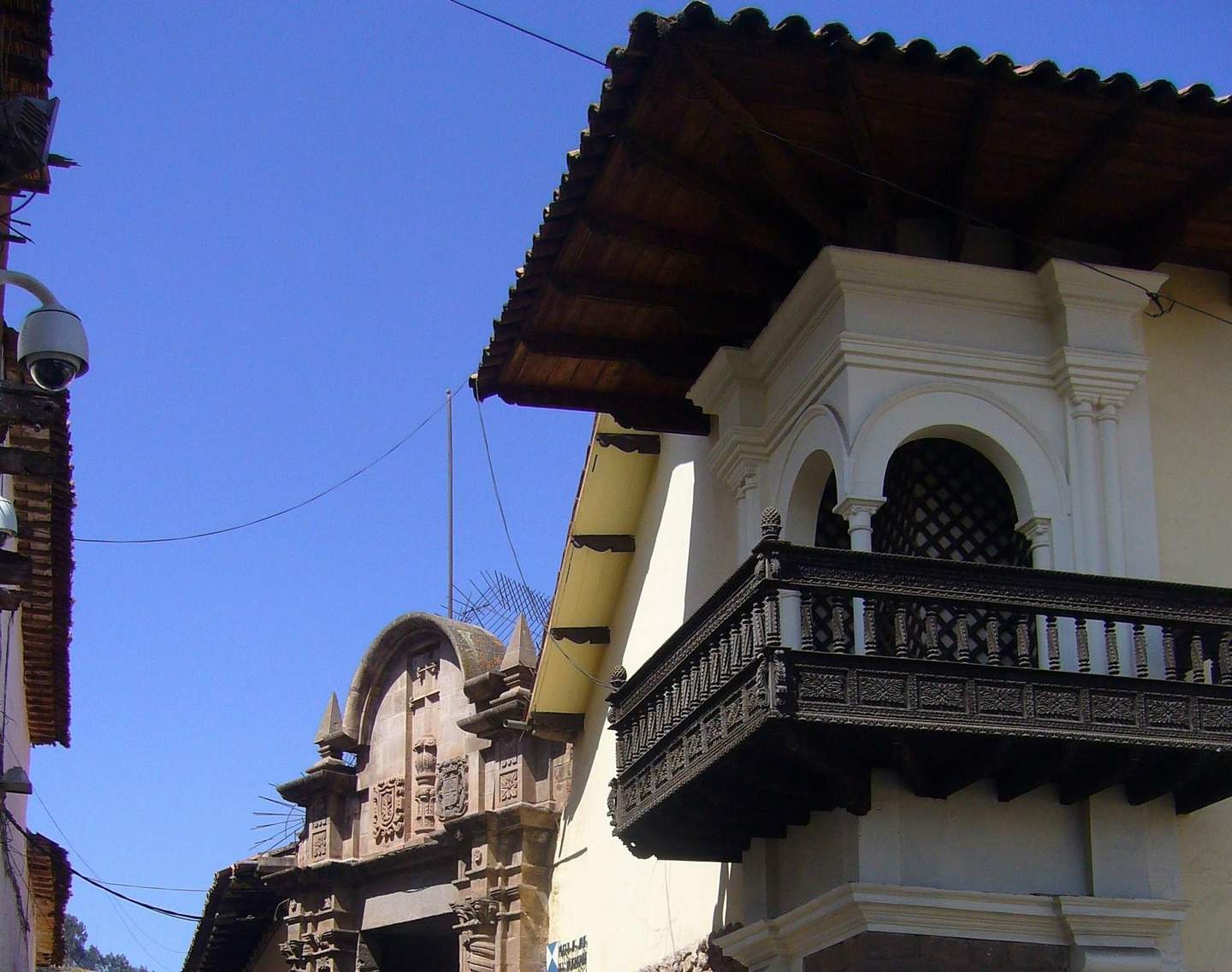 Museo de Arte Religioso - Palacio Arzobispal Colonial-style balcony with intricate woodwork next to a historic stone archway under a clear blue sky.
