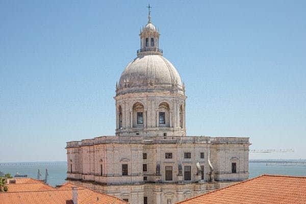National Pantheon Historic white dome with arched windows above a rectangular building, surrounded by terracotta rooftops, and a clear blue sky.