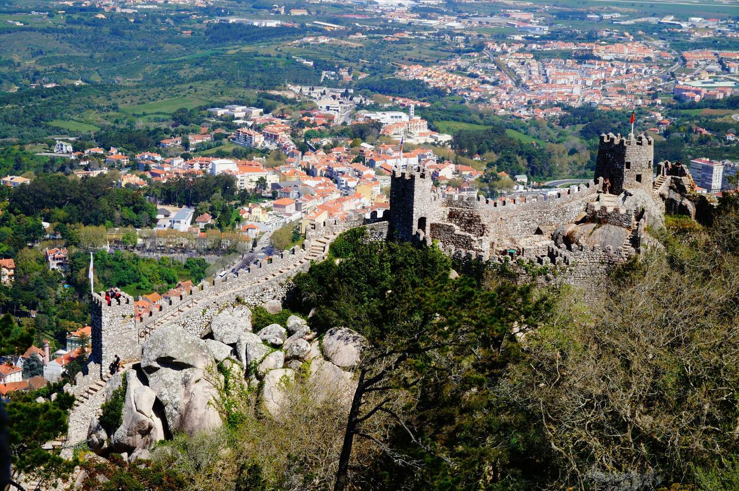 Ancient stone castle walls on a hilltop with a view of a town and green landscape below.