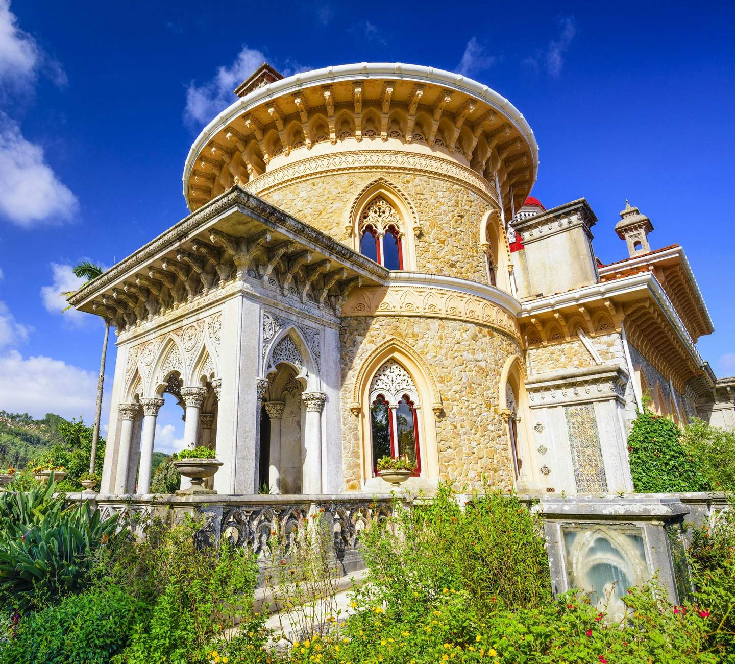 Monserrate Palace Ornate, stone building with arched windows and intricate architectural details, surrounded by lush greenery under a bright blue sky.