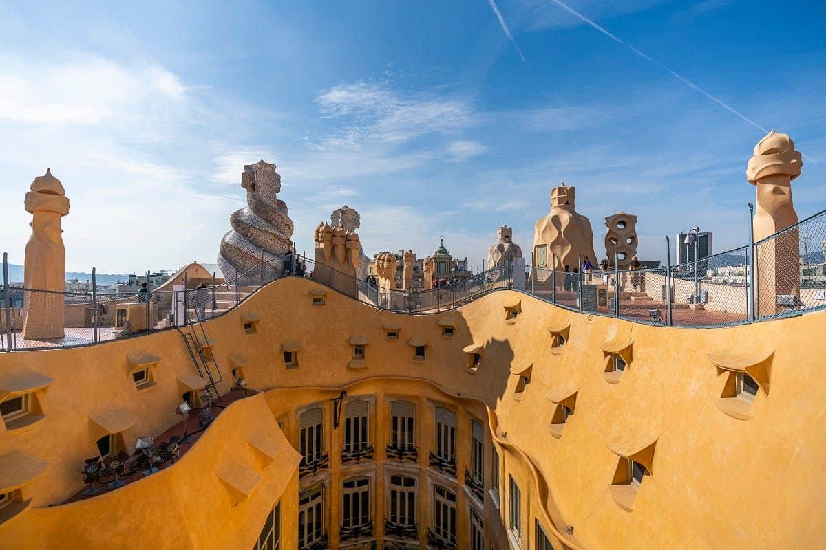 Casa Milà - La Pedrera Rooftop of a Gaudí-designed building with sculptural chimneys and yellow, wavy walls under a clear, blue sky.