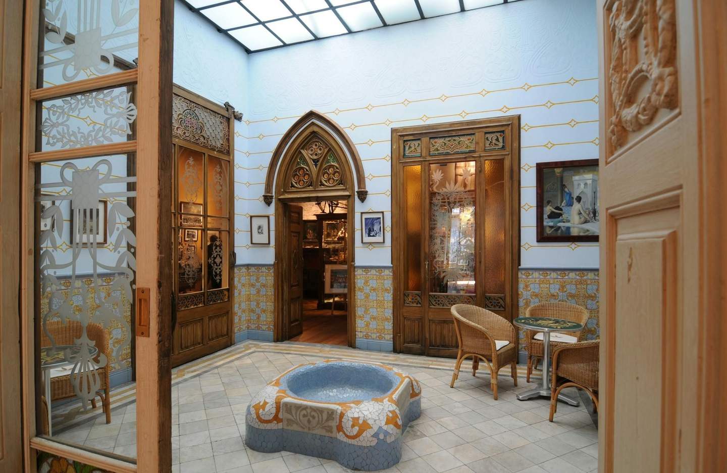 Hash Marihuana & Hemp Museum Barcelona A decorative atrium with tiled walls and floors, a mosaic fountain, wicker chairs, and glass-paneled wooden doors.