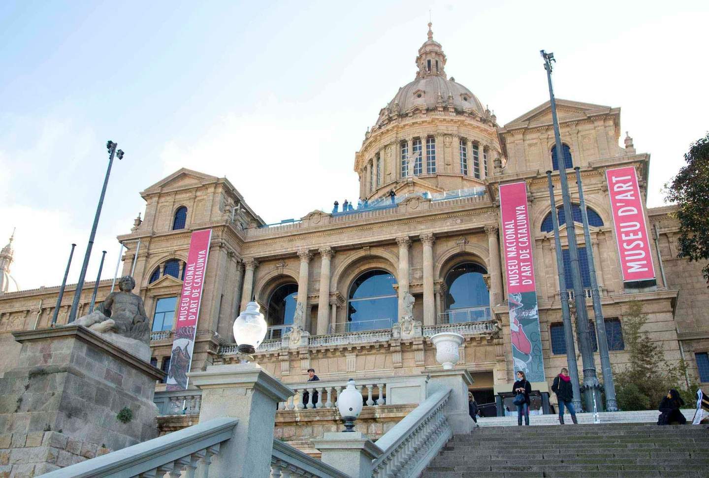 Museu Nacional d’Art de Catalunya Front view of the Museu Nacional d'Art de Catalunya, featuring large banners, stone columns, and a staircase with people.