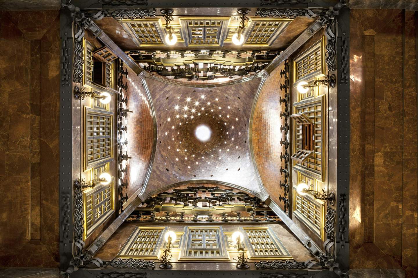Palau Güell (Güell Palace) Ornate, symmetrical interior view of a domed ceiling with intricate ironwork, glowing lamps, and wooden lattice windows.