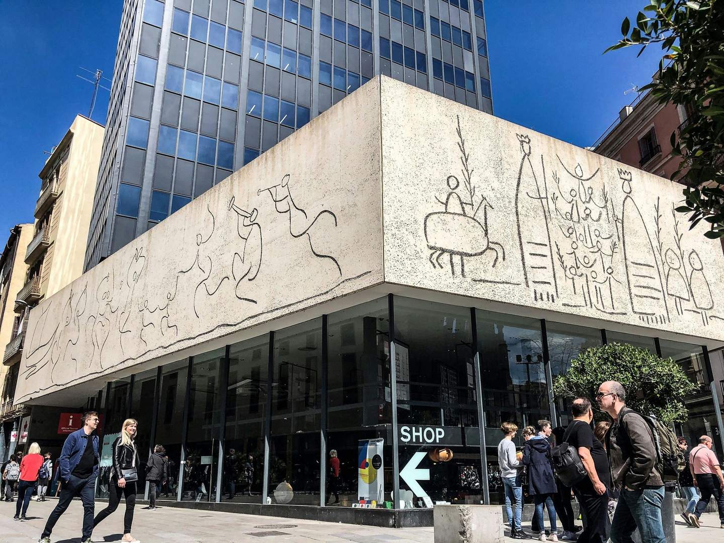 Picasso Museum A modern building with line drawings on the facade, people walking by, and a glass-fronted shop at street level.
