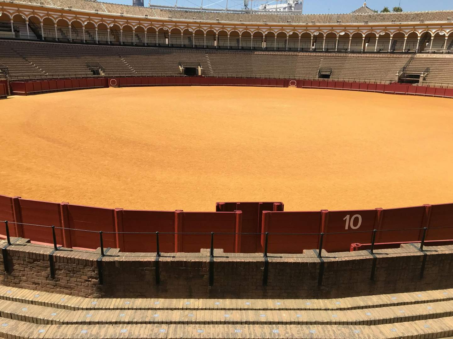 Plaza de Toros de la Real Maestranza de Caballería de Sevilla An empty bullring with a sandy arena, red barriers, and tiered seating. Marked section "10" is visible.