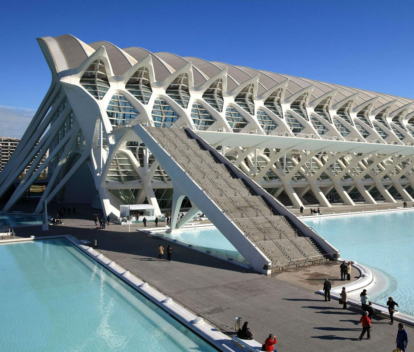 Ciudad de las artes y las ciencias Modern white building with an intricate design, adjacent to reflective pools of water; people walking and gathering nearby.