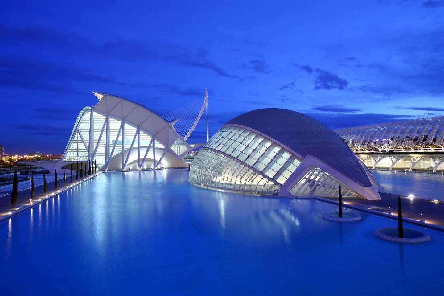 Hemisfèric Modern futuristic buildings with white structures and large glass windows, surrounded by a reflecting pool under a twilight sky.