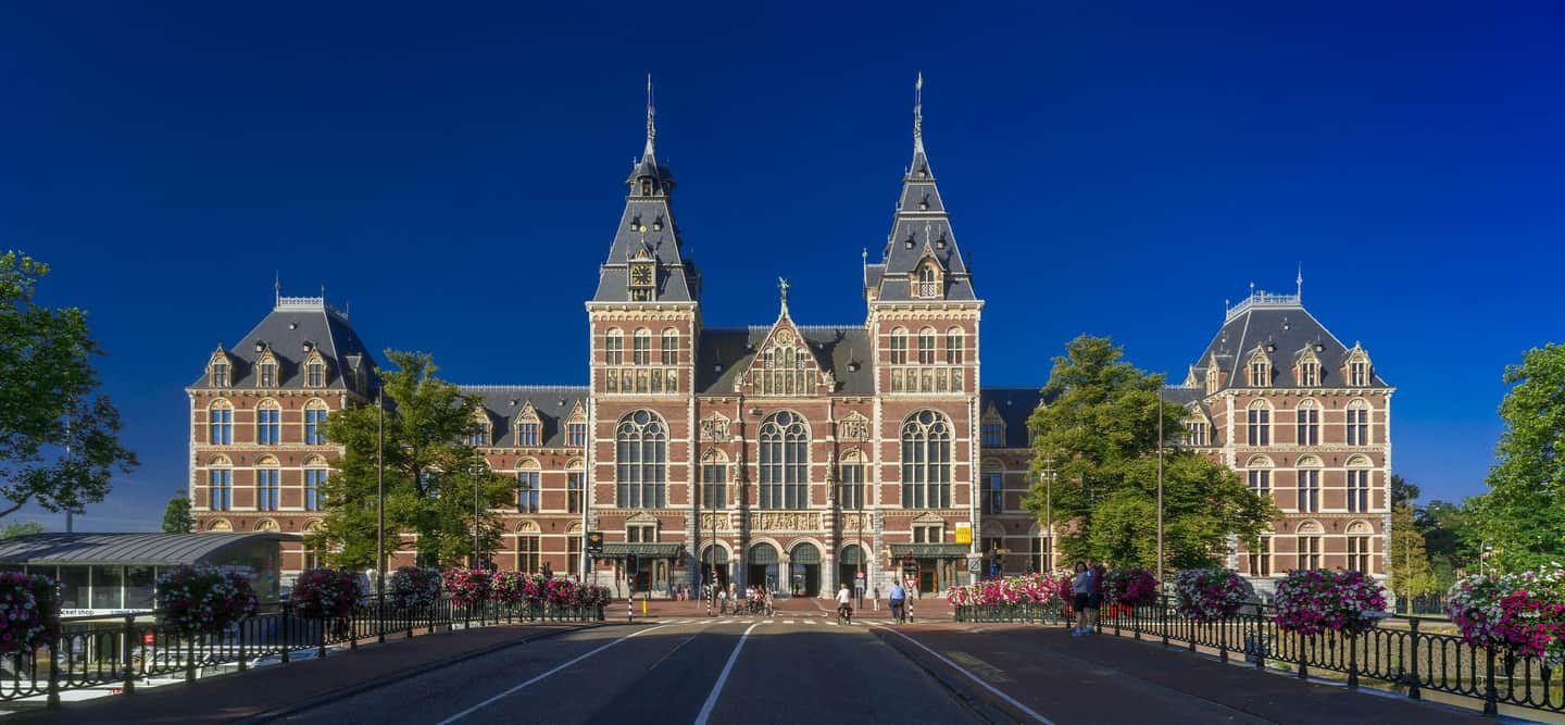 Rijksmuseum A grand, gothic-style building with multiple towers and arched windows, viewed from a street with flowers and trees.