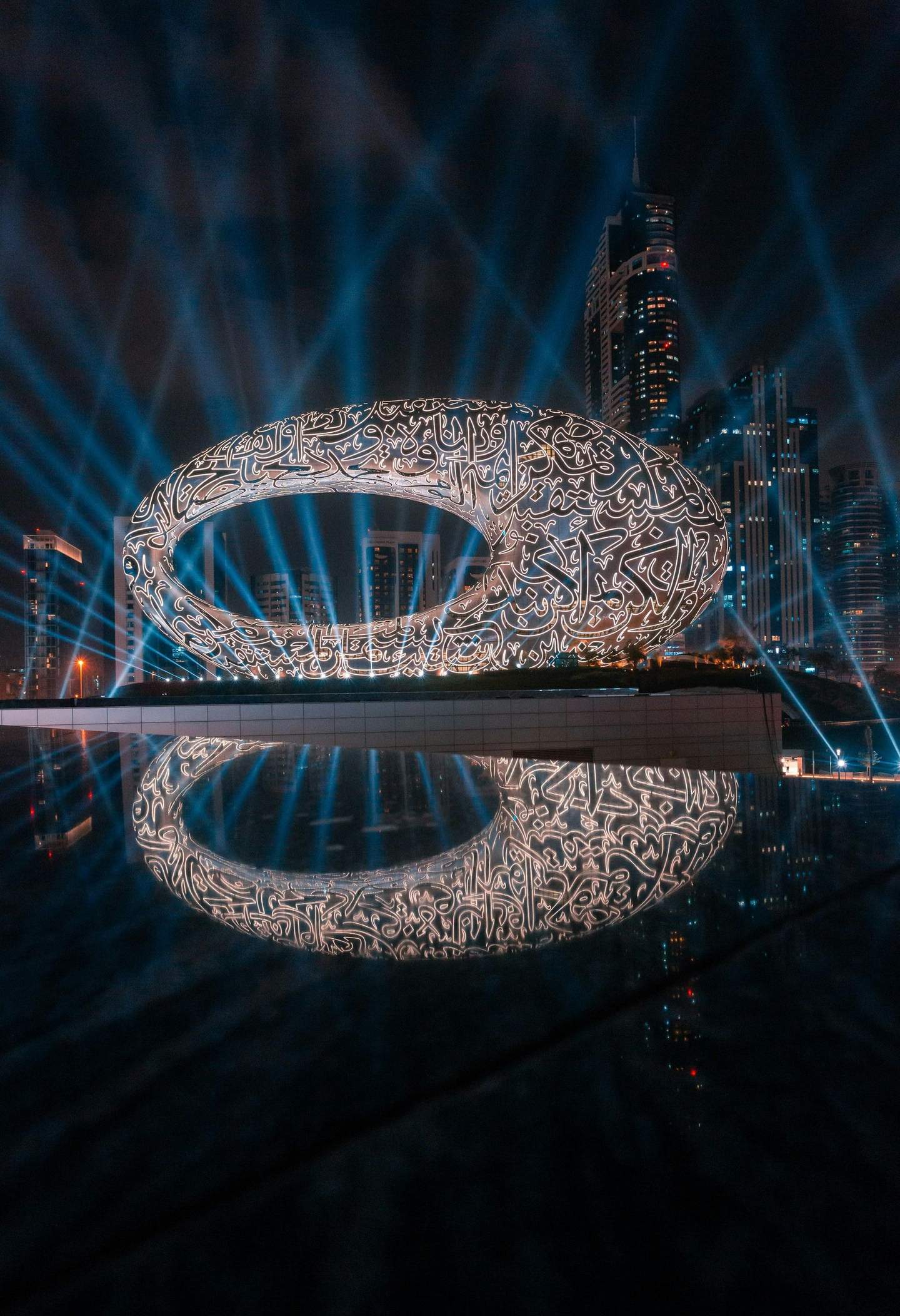 Museum of the Future A futuristic oval-shaped building with glowing script patterns, set against a cityscape with skyscrapers and illuminated by blue beams.