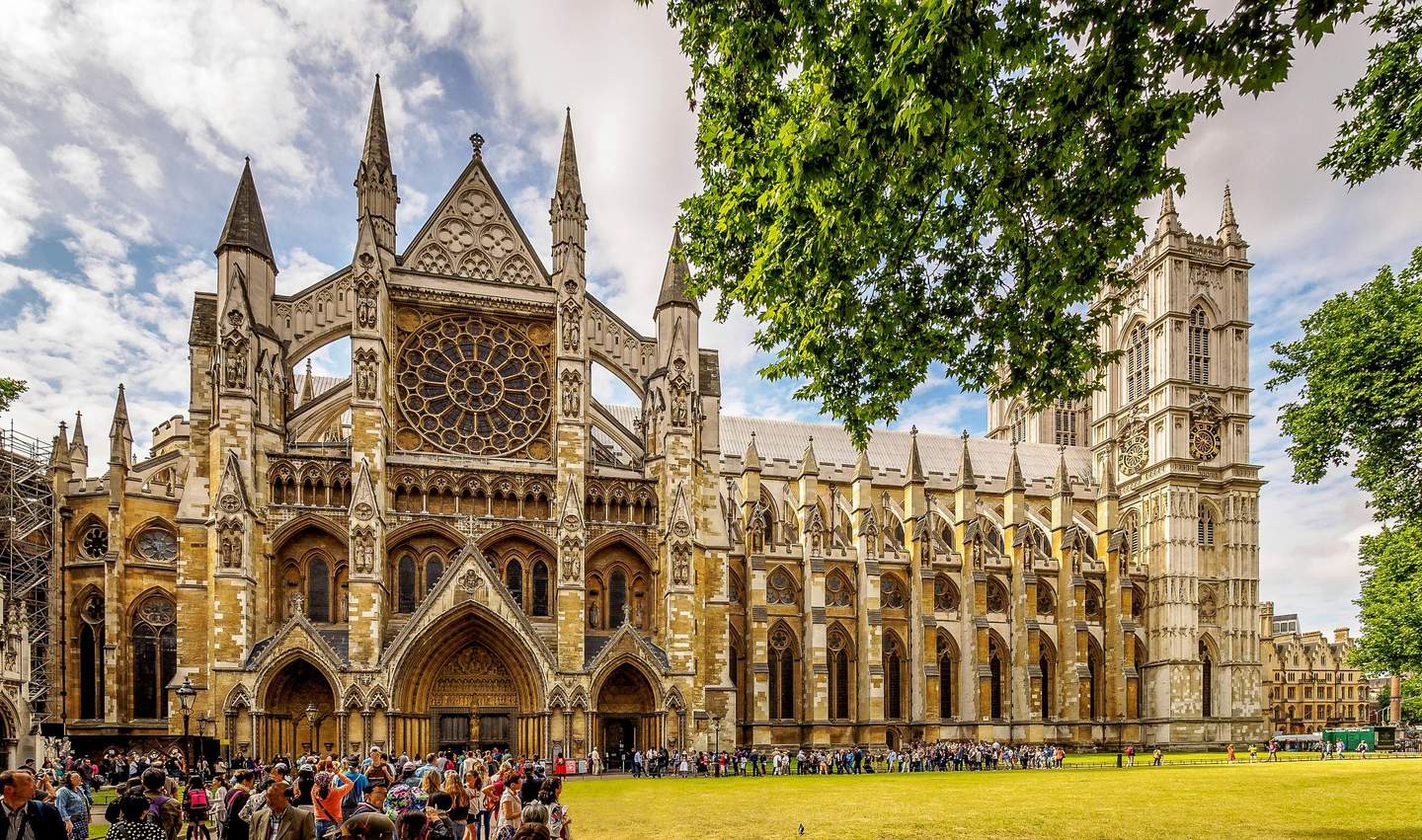 Westminster Abbey A large Gothic cathedral with detailed architecture and a rose window, surrounded by trees and people gathered outside.
