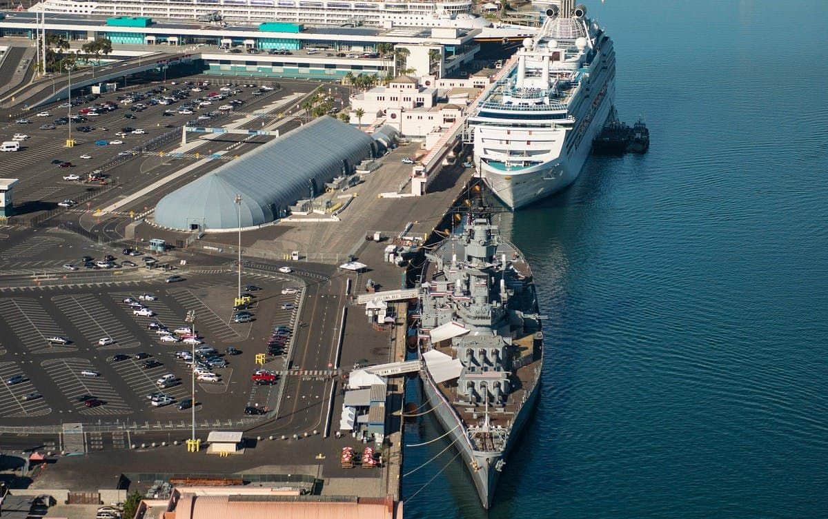 Battleship IOWA Aerial view of a cruise ship and a battleship docked at a port with adjacent parking lots and terminal buildings.