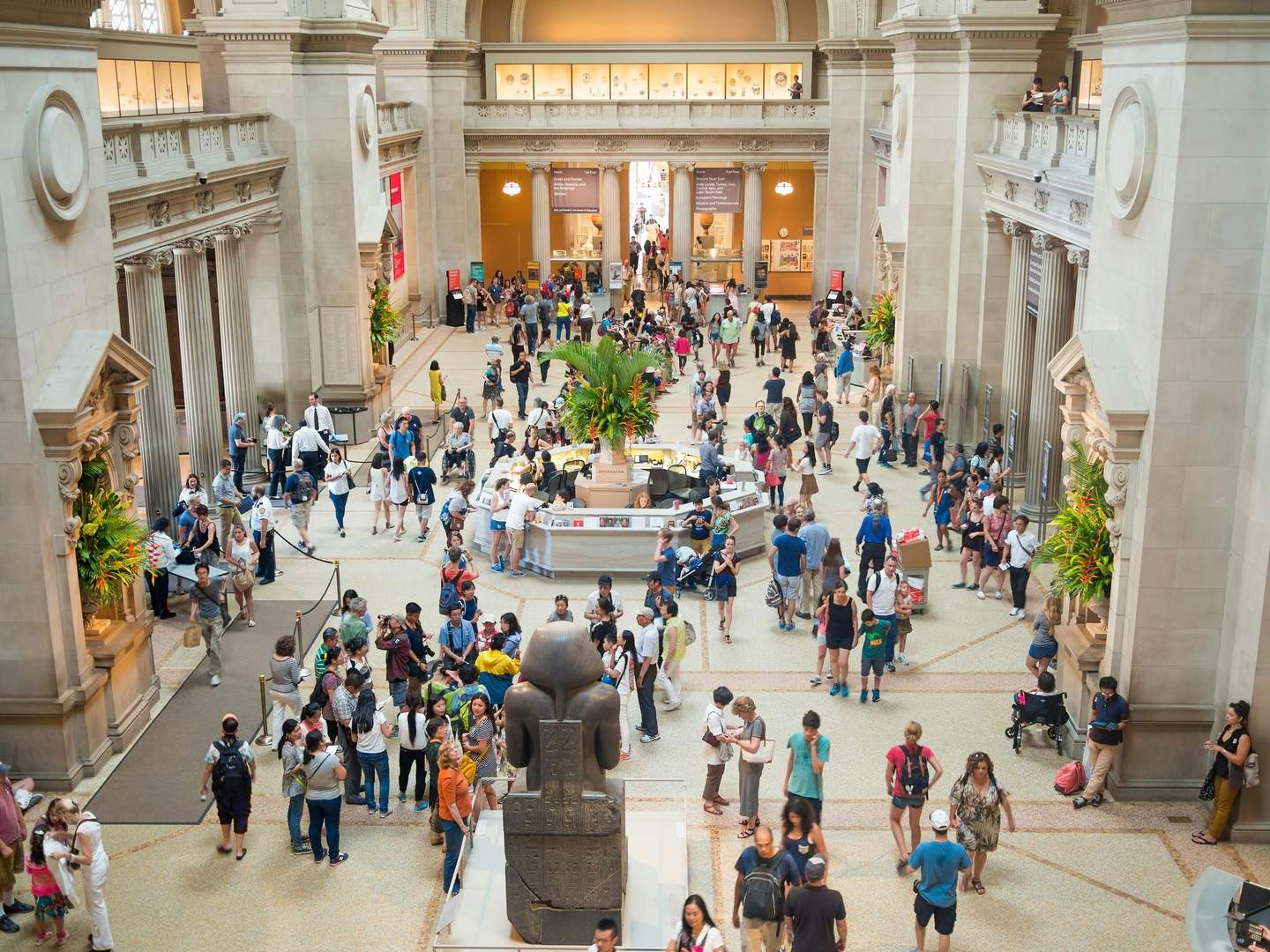 The Metropolitan Museum of Art A large, bustling museum hall filled with visitors exploring exhibits and gathering near an information desk.
