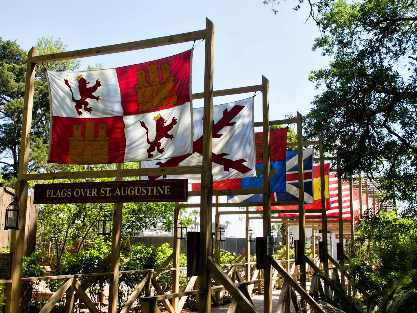 Colonial Quarter A display of various historical flags in a wooded area with a sign reading "Flags Over St. Augustine."