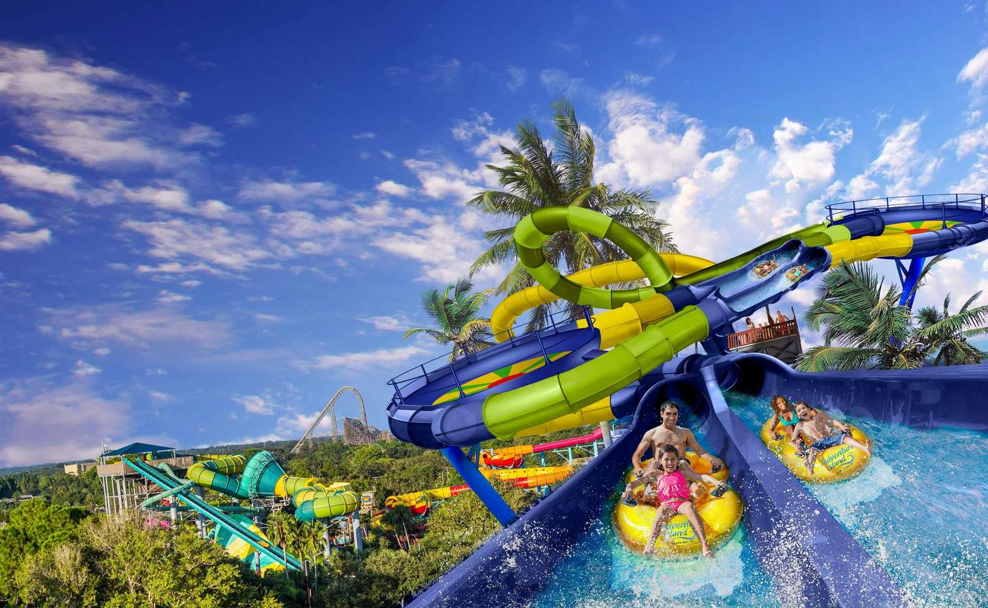 People sliding down brightly colored water slides among palm trees under a clear blue sky at a water park.