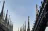 Neo-Gothic spires and statues atop the Milan Cathedral, set against a blue sky.