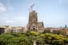 Vue aérienne de la basilique de la Sagrada Familia à Barcelone, entourée d'arbres et d'immeubles, avec une grue visible au sommet.