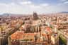 Vue aérienne d'un paysage urbain dense avec une grande cathédrale caractéristique au centre, sous un ciel partiellement nuageux.